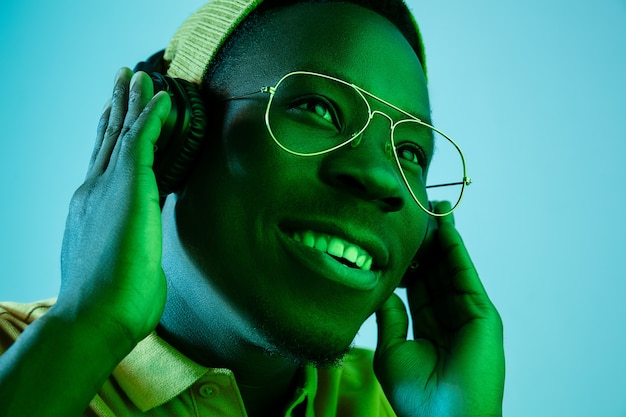 Der junge gutaussehende glückliche überraschte Hipster-Mann, der Musik mit Kopfhörern im Studio mit Neonlichtern hört. Disco, Nachtclub, Hip-Hop-Stil, positive Emotionen, Gesichtsausdruck, Tanzkonzept