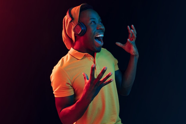 Der junge hübsche glückliche Hipster-Mann, der Musik mit Kopfhörern im schwarzen Studio mit Neonlichtern hört