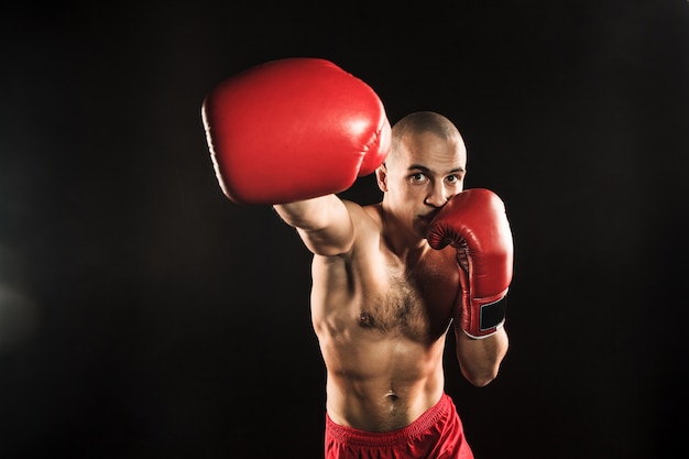 Der junge männliche Athlet tritt auf einem schwarzen Kickboxen