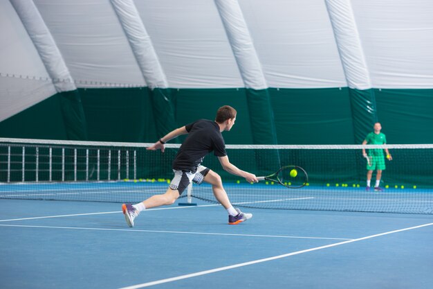 Der junge Mann auf einem geschlossenen Tennisplatz mit Ball