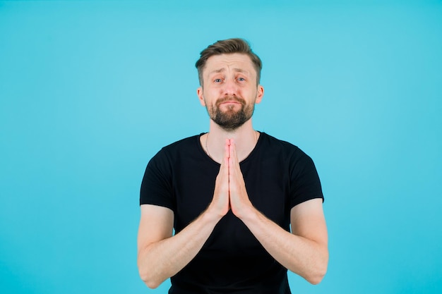 Kostenloses Foto der junge mann bettelt, indem er die hände auf blauem hintergrund zusammenhält