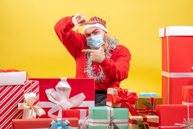 Der junge Mann der Vorderansicht, der herum sitzt, präsentiert in der sterilen Maske auf gelbem Hintergrund