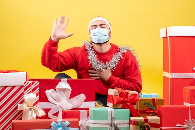 Der junge Mann der Vorderansicht, der herum sitzt, präsentiert in der sterilen Maske auf gelbem Hintergrund