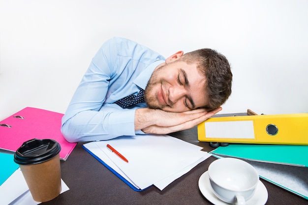Der junge Mann schläft dreist während seiner Arbeitszeit auf dem Schreibtisch