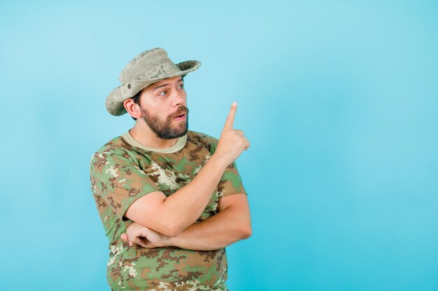 Der junge Offizier zeigt mit dem Zeigefinger auf blauem Hintergrund nach oben