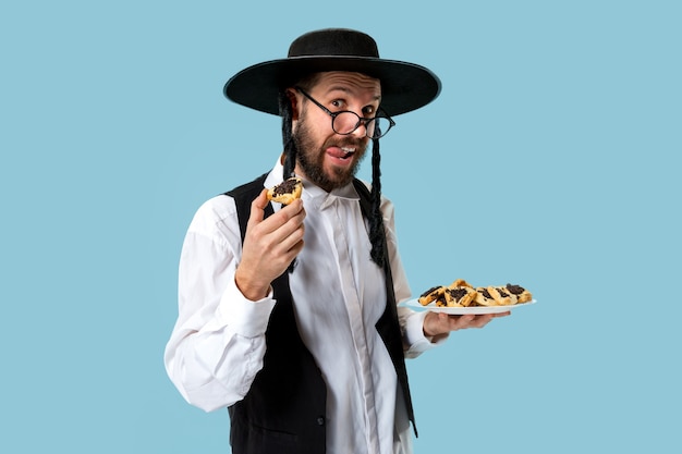 Der junge orthodoxe jüdische Mann mit Hamantaschen-Keksen für das Festival Purim. Feiertag, Feier, Judentum, Gebäck, Tradition, Keks, Religionskonzept