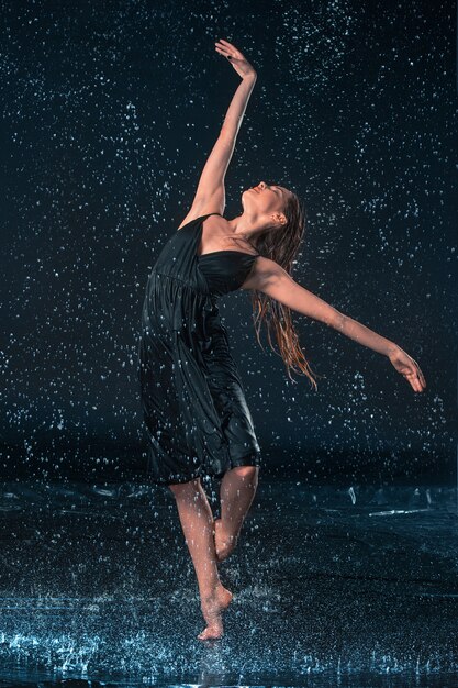 Der junge schöne moderne Tänzer, der unter Wassertropfen tanzt