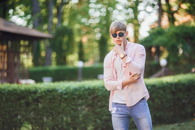 Der junge stylische gutaussehende Kerl in Freizeitkleidung und Sonnenbrille und Uhr steht auf dem Campus