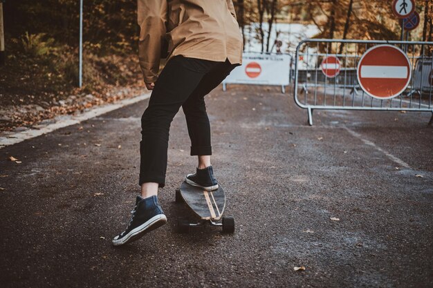 Der junge trendige Mann fährt mit seinem Longboard im Herbstpark, umgeben von gelben Bäumen.