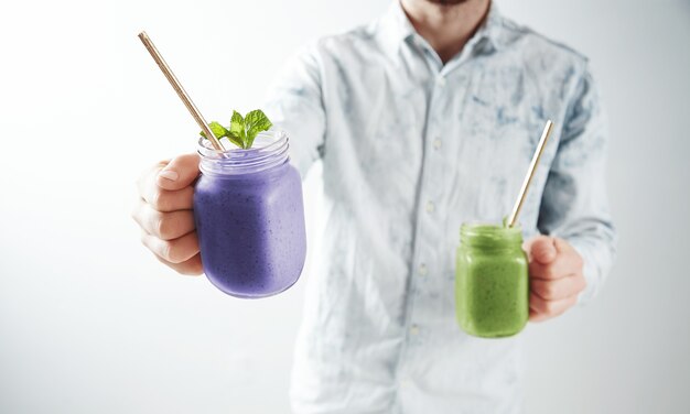 Der Kellner bietet zwei leckere kalte Smoothies aus Blaubeeren und Kiwi in rustikalen Gläsern mit Trinkhalm an