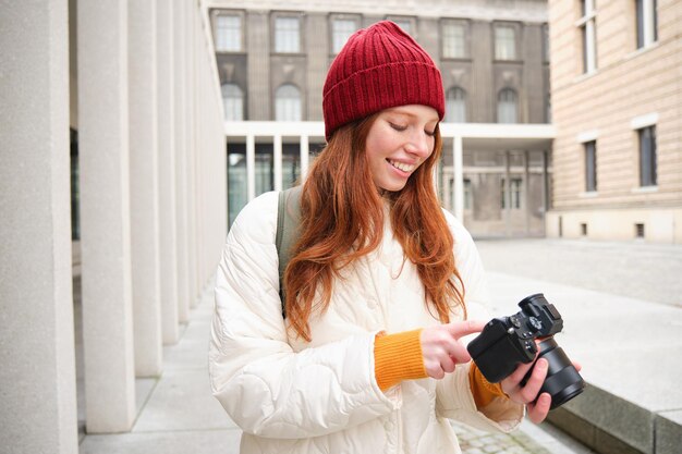 Der lächelnde Fotograf des rothaarigen Mädchens, der Fotos in der Stadt macht, macht Fotos im Freien auf einem professionellen Foto