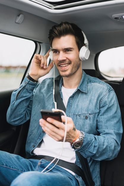 Der lächelnde junge Mann, der die Musik auf dem Kopfhörer genießt, befestigt zum Mobiltelefon