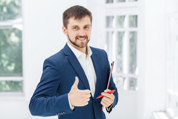 Der lächelnde männliche Büroangestellte gegen weißes Büro