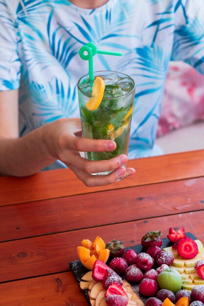 Der Mann, der Mojito-Cocktail hält, diente mit Servierplatte der exotischen Frucht