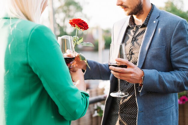 Der Mann, der seiner Freundin rote Rose gibt, während Wein trinkend