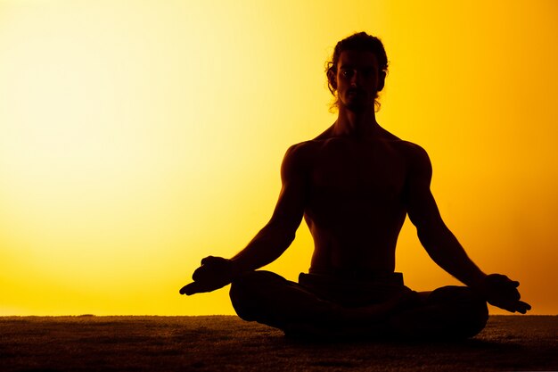 Der Mann, der Yoga im Sonnenuntergangslicht praktiziert
