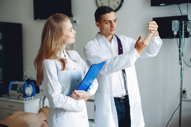 Der Mann hält eine Flasche zur Analyse in der Hand. Die Krankenschwester mit einem Ordner in der Hand hört dem Arzt zu. Die Studenten in Krankenhauskitteln.