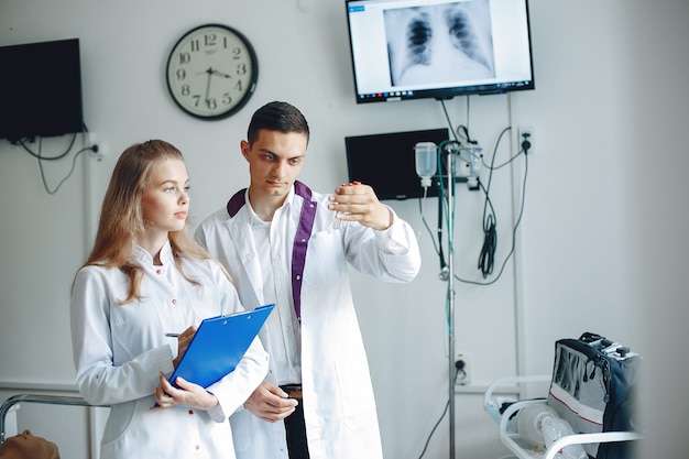 Der Mann hält eine Flasche zur Analyse in der Hand. Die Krankenschwester mit einem Ordner in der Hand hört dem Arzt zu. Die Studenten in Krankenhauskitteln.