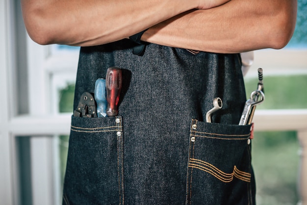 Der Mechaniker trägt eine schwarze Schürze und in der Tasche befinden sich Handwerkzeuge.