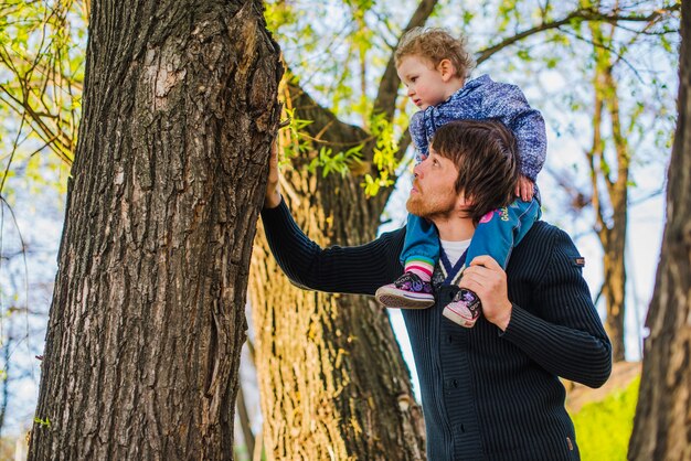 Der Mensch berührt einen Koffer mit seinem Sohn, der auf seinen Schultern sitzt