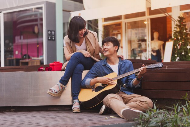 Der Mensch in der Liebe spielt Gitarre auf dem Boden zu seiner Freundin sitzen