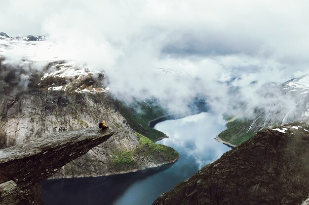 Der Mensch sitzt am Ende von Trolltunga vor den Bergen