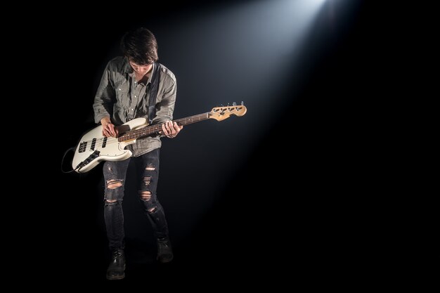 Der Musiker spielt Bassgitarre auf einem schwarzen Hintergrund mit einem Lichtstrahl, emotionales Spiel, Musikkonzept