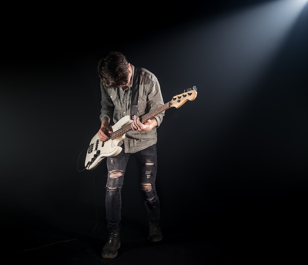 Der Musiker spielt Bassgitarre auf einem schwarzen Hintergrund mit einem Lichtstrahl