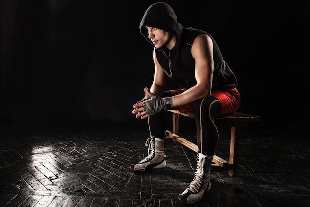 Der muskulöse Boxer sitzt und ruht auf Schwarz