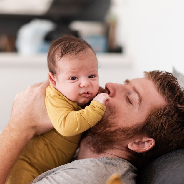 Der Nahaufnahmevater, der Baby küsst, kleidete im Gelb an