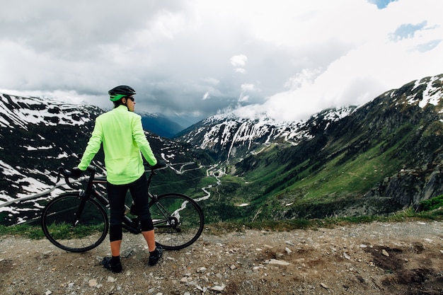 Der Radfahrer, der mit Straße steht, fährt auf Hintergrund der schönen alpinen Gebirgslandschaft rad