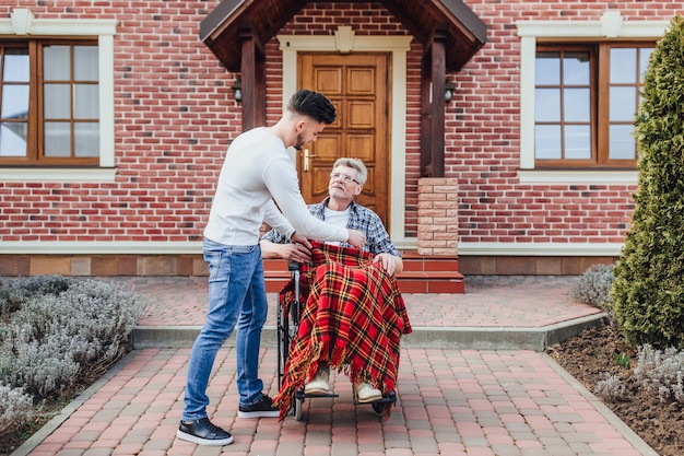 Der Sohn hilft seinem Vater im Rollstuhl in der Nähe des Pflegeheims