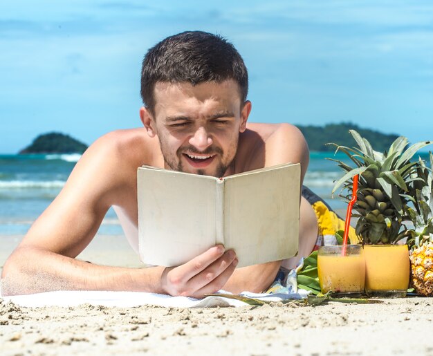 der Typ, der am Strand liegt und ein Buch vor dem Hintergrund des Sommers liest