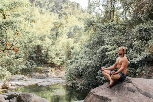 Der Typ meditiert auf einem Stein im Wald