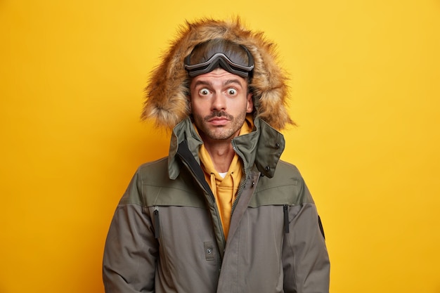 Der überraschte junge Mann mit der Snowboardbrille starrt die Augen an, die von einem stürmischen Schneesturm in Winteroberbekleidung betäubt sind.