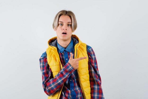 Der überraschte Teenager zeigt mit dem Zeigefinger auf weißem Hintergrund nach rechts