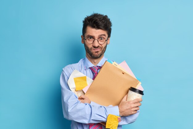 Der unzufriedene, überarbeitete Student arbeitet hart, bevor die Prüfungssitzung eine Tasse Kaffee zum Einweg hält und die Papiere sich an die Frist erinnern, in der sie formelle Kleidung tragen
