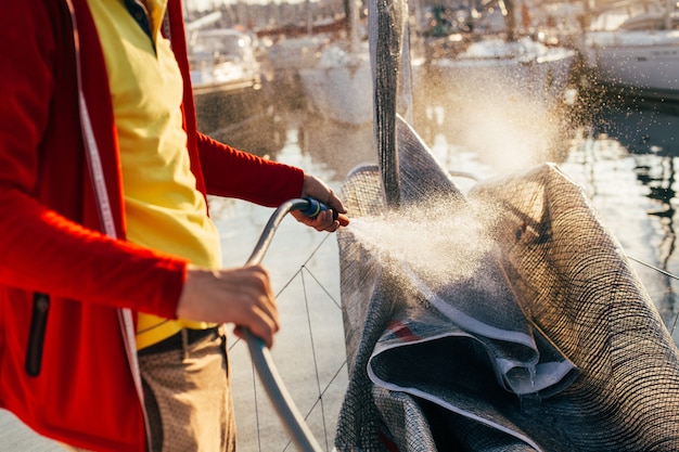 Der weiche Fokus von Wassertropfen kommt aus dem Schlauch, dem Seemann oder dem Kapitän. Der Yachtbesitzer wäscht salzige Rückstände vom Segel, Großsegel oder Spinnaker, wenn das Segelboot im Hof oder in der Marina angedockt ist