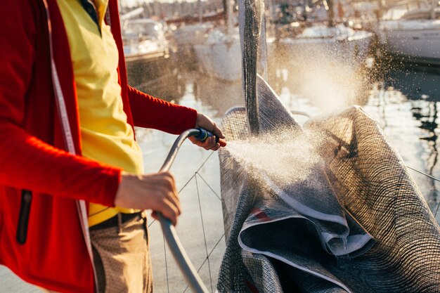 Der weiche Fokus von Wassertropfen kommt aus dem Schlauch, dem Seemann oder dem Kapitän. Der Yachtbesitzer wäscht salzige Rückstände vom Segel, Großsegel oder Spinnaker, wenn das Segelboot im Hof oder in der Marina angedockt ist