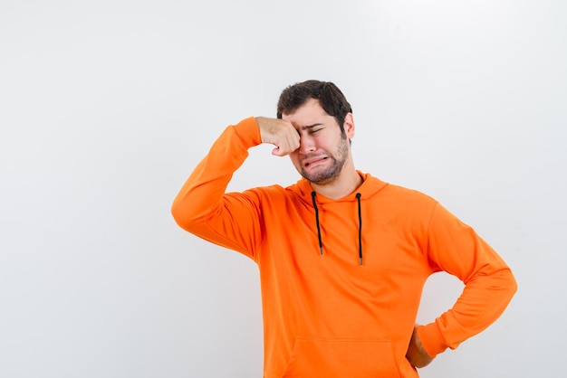 Der weinende Mann hält seine Hand auf dem Auge und legt die andere auf die Taille auf weißem Hintergrund