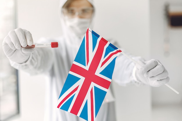 Der Wissenschaftler im Overallanzug mit Coronavirus-Probe und britischer Flagge