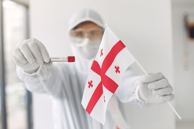 Der Wissenschaftler im Overallanzug mit Coronavirus-Probe und georgischer Flagge