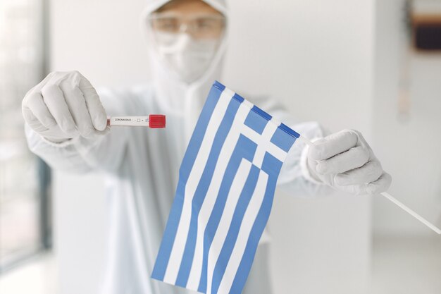 Der Wissenschaftler im Overallanzug mit Coronavirus-Probe und griechischer Flagge
