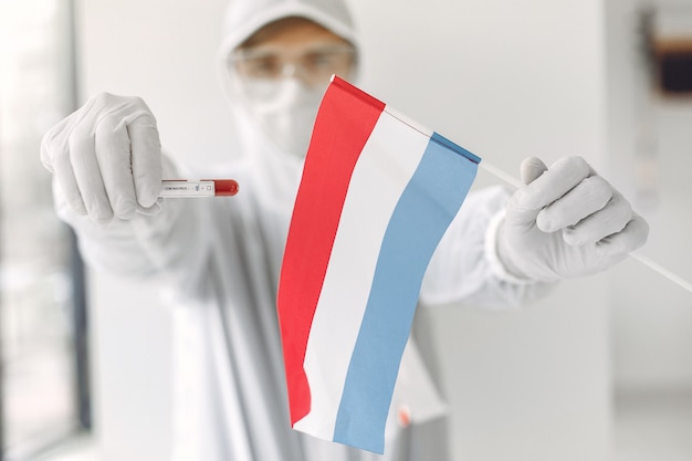 Der Wissenschaftler im Overallanzug mit einer Coronavirus-Probe und der niederländischen Flagge