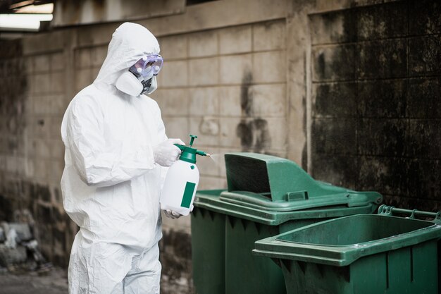 Desinfektionsfachmann in Schutzanzug, Handschuhen, Maske und Gesichtsschutz, Reinigung des Quarantänebereichs mit einer Flasche Druckdesinfektionsmittel zur Entfernung des Coronavirus