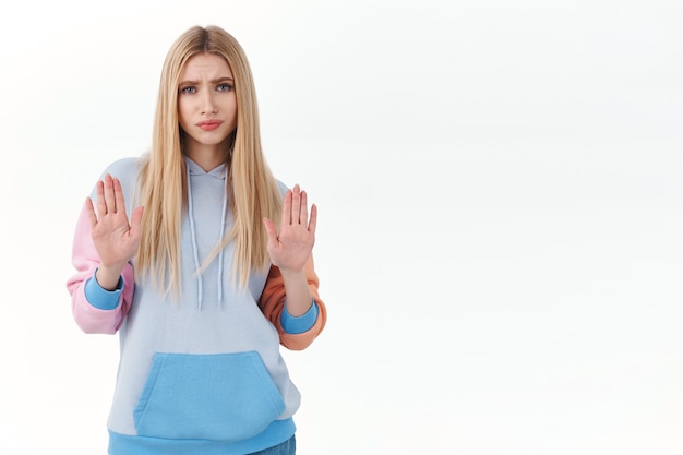 Desinteressiertes, skeptisches blondes Mädchen im Teenageralter, das Stoppschild zeigt, die Hände hebt