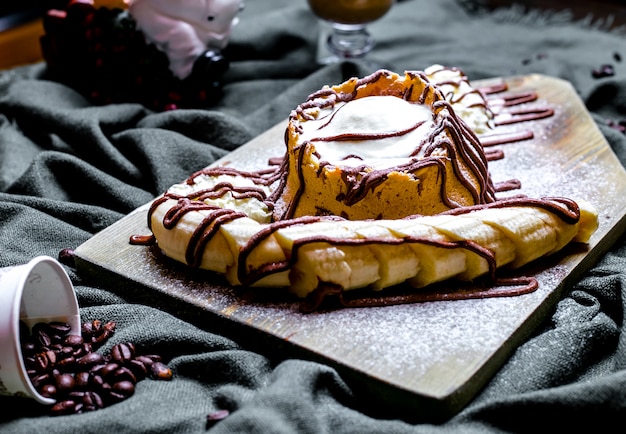 Dessert von oben mit Eiscreme und Schlagsahne, garniert mit geschnittener Banane und gegossener Schokolade auf dem Brett