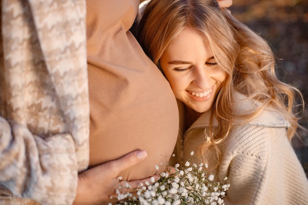 Detailansicht des glücklichen Mädchens in der Nähe eines schwangeren Bauches Frauen, die ein Baby erwarten und in einem Park im Herbst stehen Portrait of lockige blonde Frau