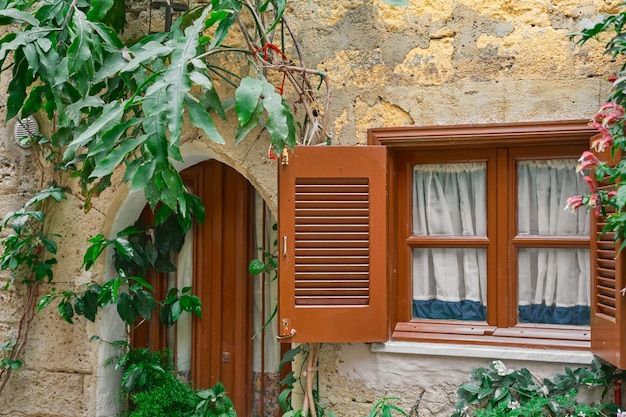 Details eines traditionellen griechischen Hauses mit Holzjalousien und Blumen am Fenster, eine Idee für einen Hintergrund oder einen Artikel über die Stadt Rhodos, einen Ausflug zu beliebten Orten