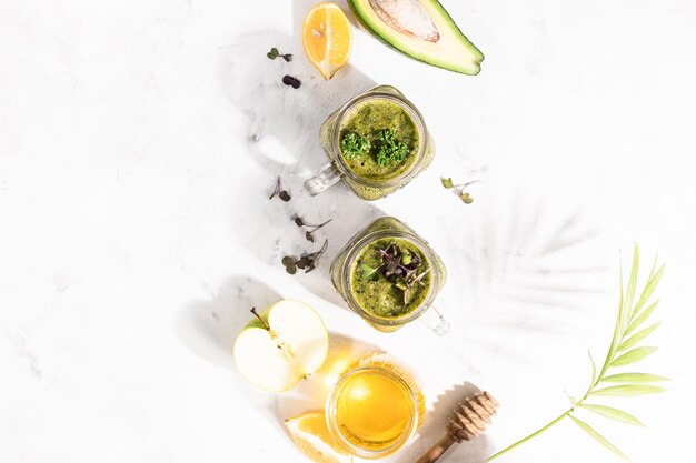 Detox Green Smoothie - Avocado, Microgreen, Zitrone und Honig auf weißem Stein- oder Betonhintergrund. Helles Licht und Schatten. Selektiver Fokus, Kopienraum. Ansicht von oben.